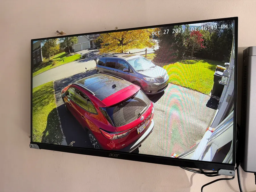 A TV showing a live camera view of a driveway with two parked cars.