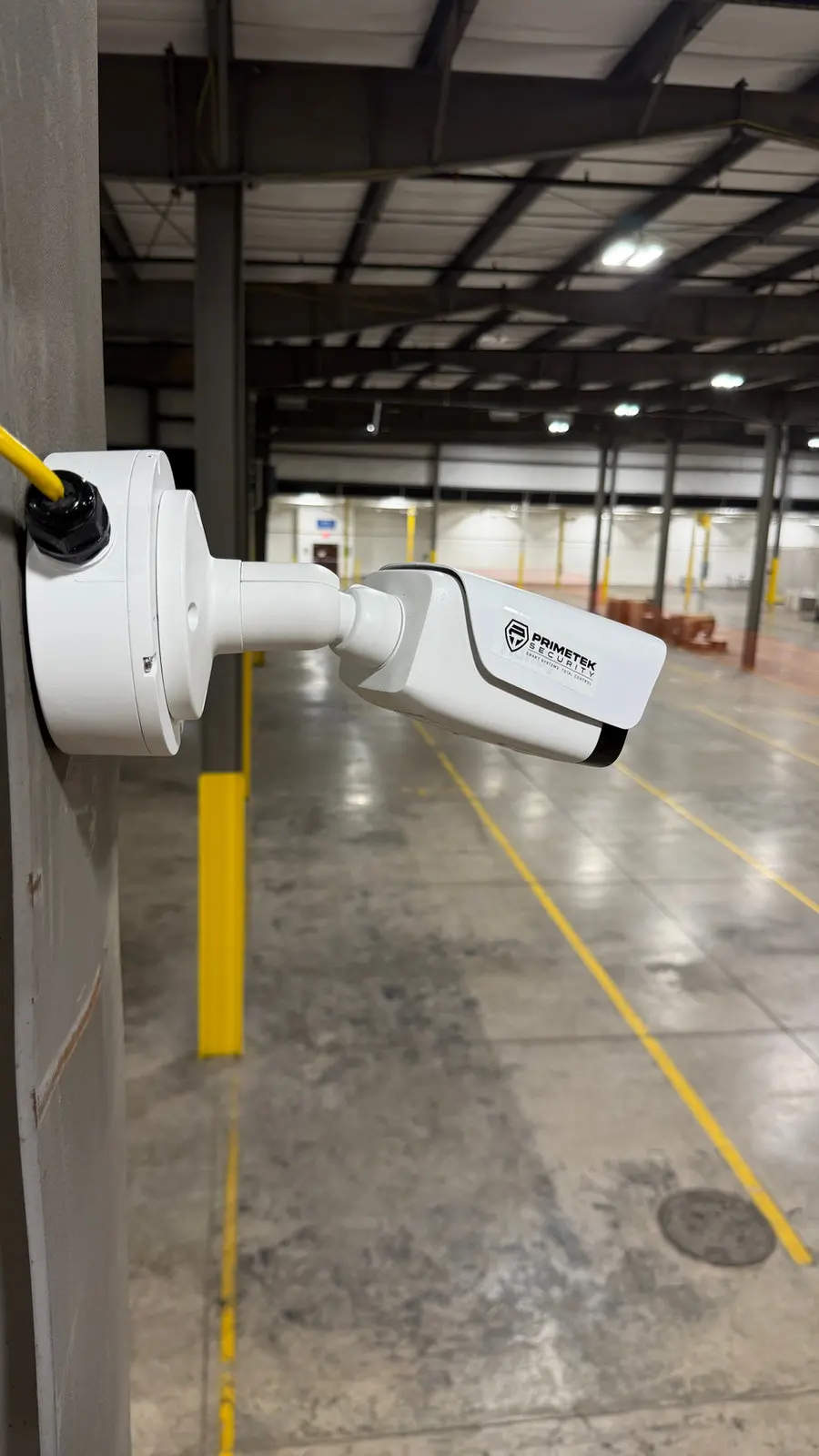 A bullet camera on a column inside a warehouse, aimed down the aisle.