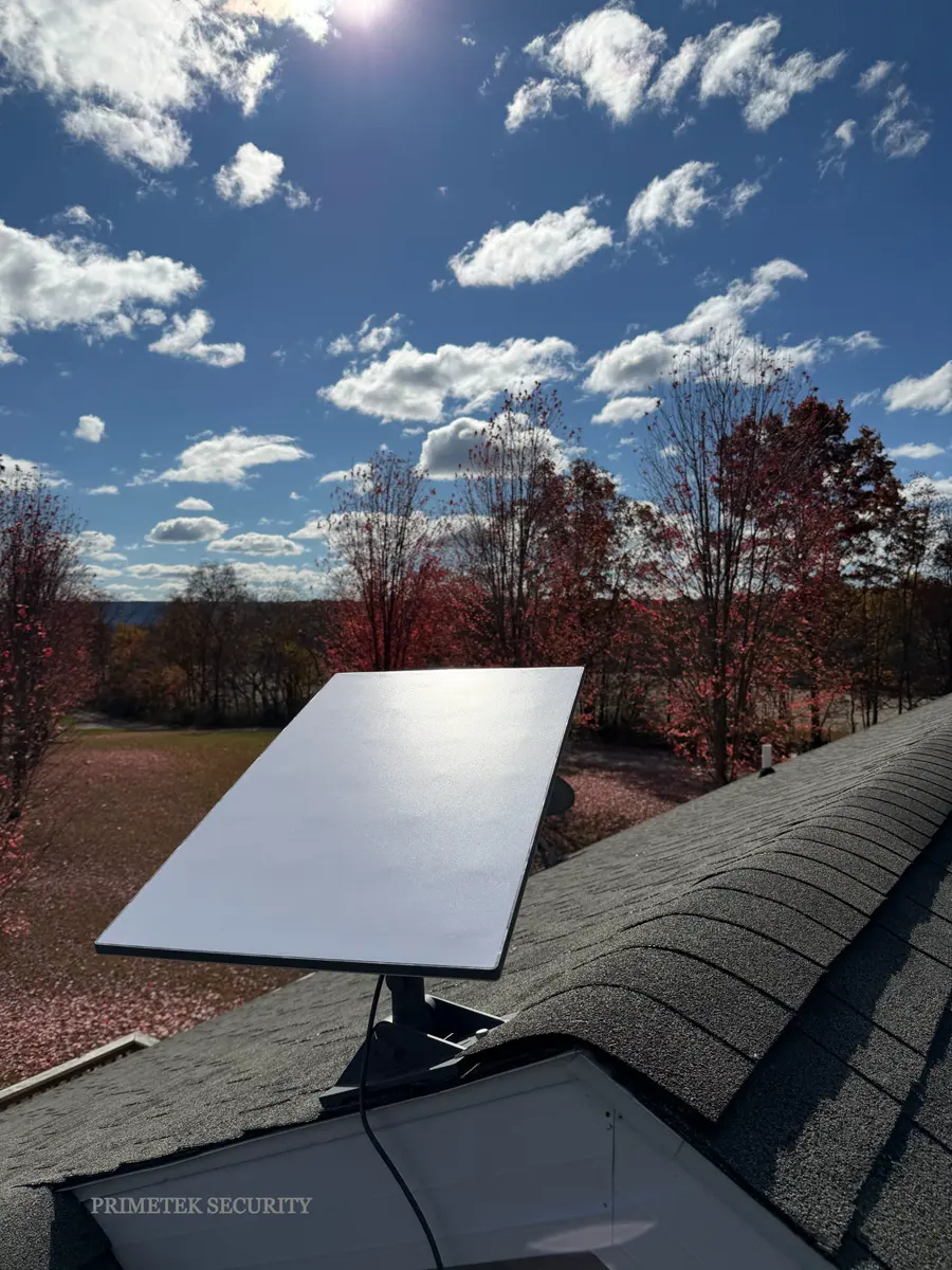 A Starlink dish on a roof ridge above autumn trees.
