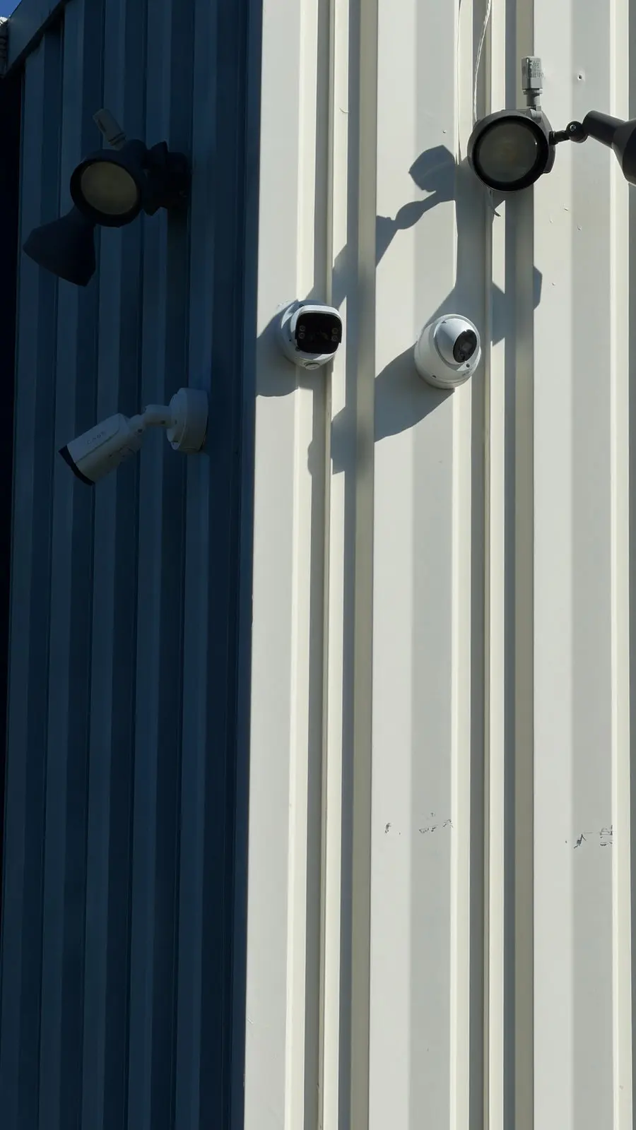 Several cameras mounted on the metal siding of a commercial building.