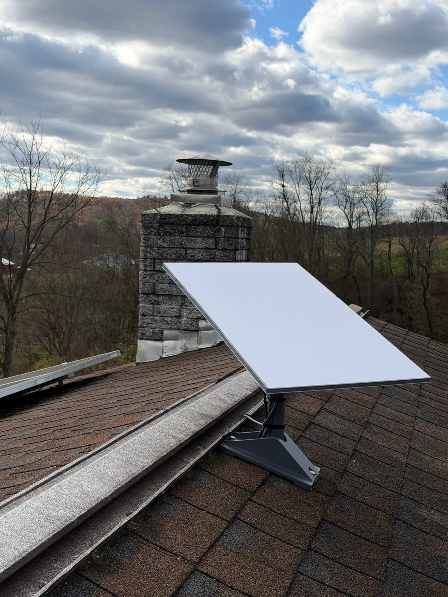 A Starlink dish on a shingle roof beside a stone chimney.