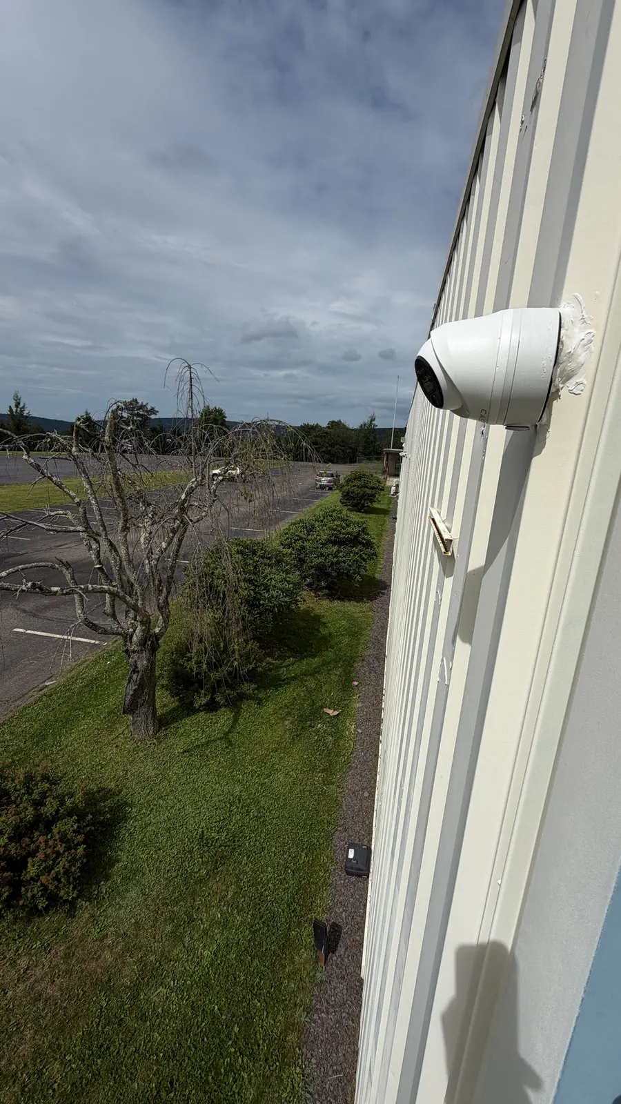 A dome camera on commercial siding overlooking a parking lot.