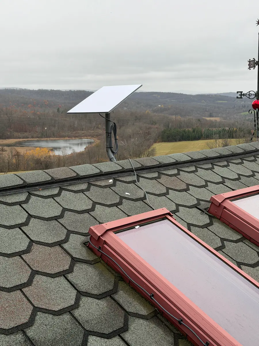 A Starlink dish on a scalloped shingle roof above two skylights, with a valley view.