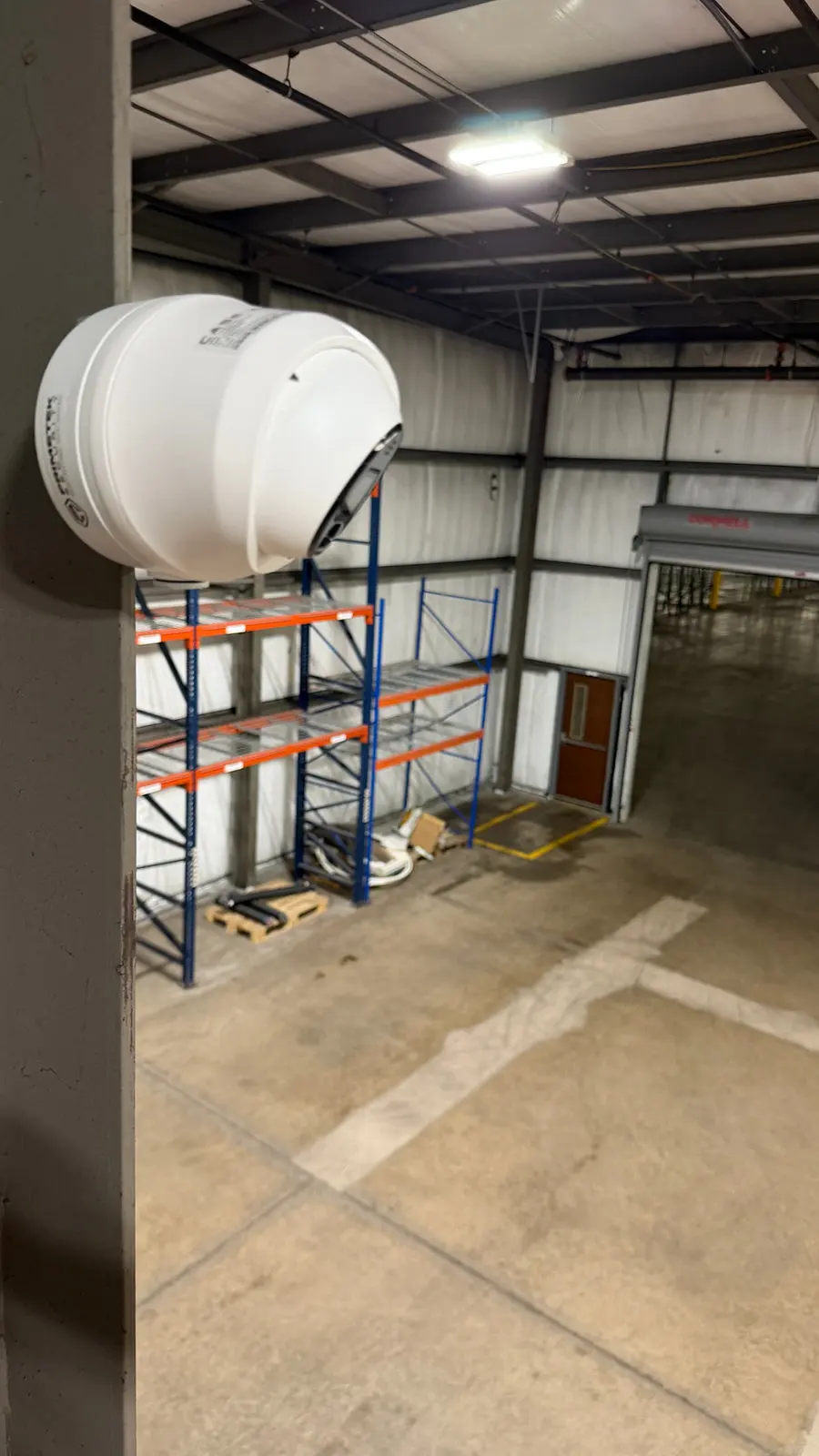 A large dome camera inside a warehouse above shelving.